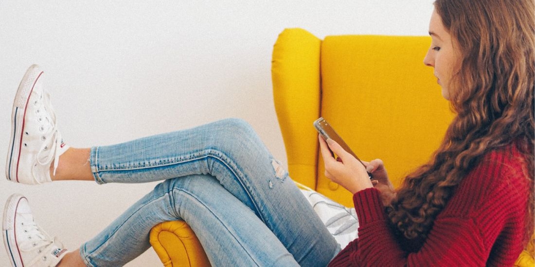 Kvinne som sitter i stol og ser på mobilen