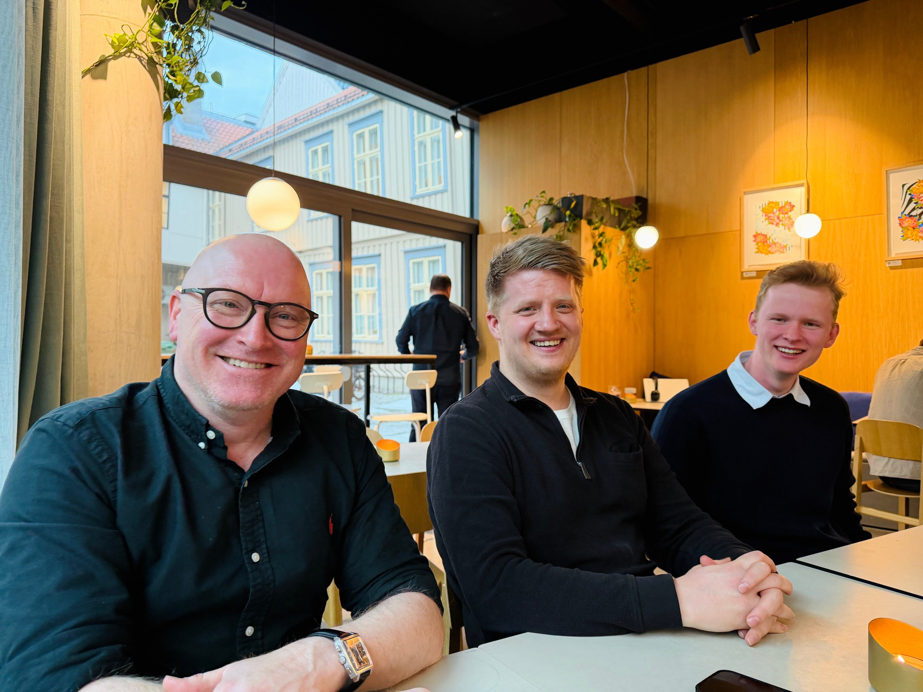 Tre mennesker som sitter ved et bord og smiler