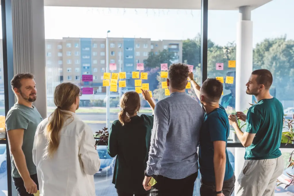 6 people using sticky notes at a glass window